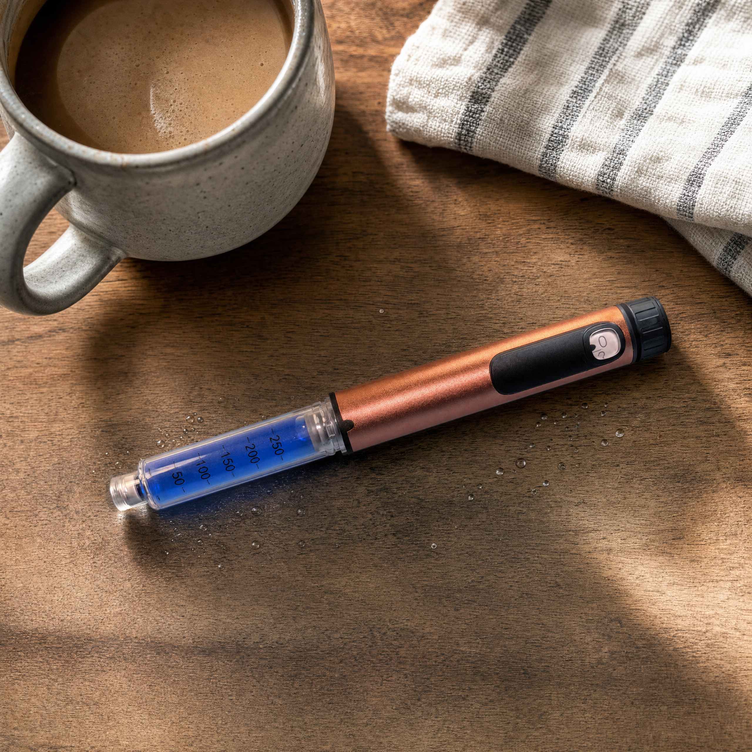 A Peptide Critic pen resting on a wood table beside a mug of coffee